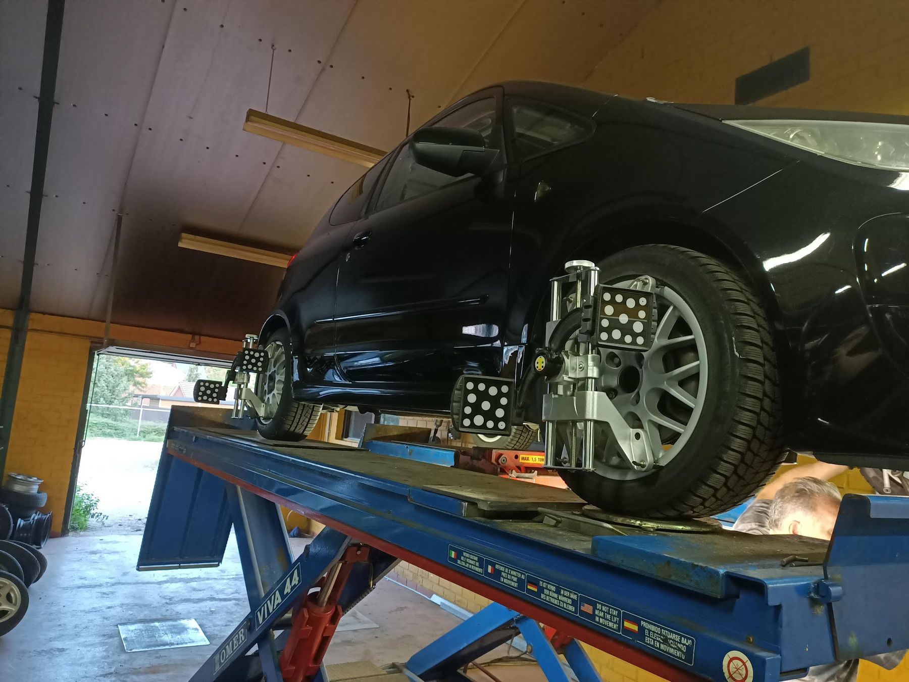 Zwarte Nissan Skyline op de uitlijnbrug in de werkplaats, met meetklemmen op de wielen