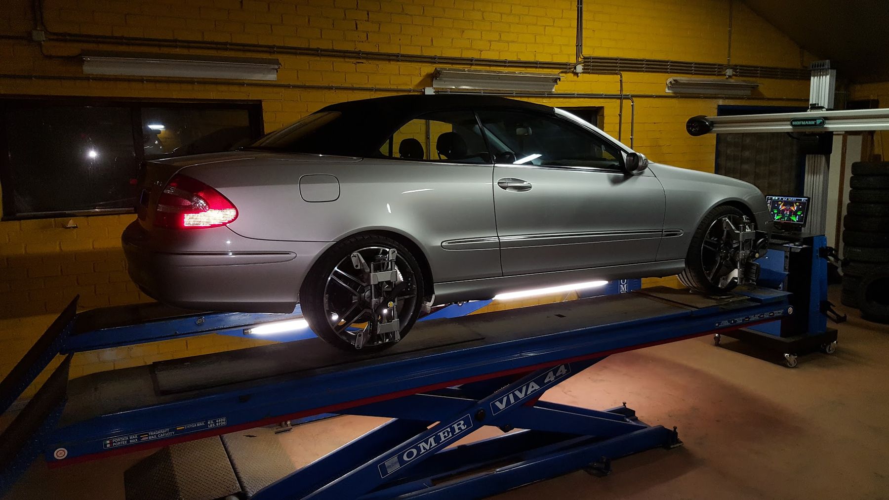 Zilveren Mercedes cabriolet op de uitlijnbrug met meetdoelen op de wielen